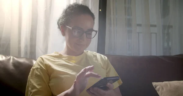 Kafkasyalı genç bir kadının Sofa 'da otururken akıllı telefon kullandığı portreyi kapat. Evde cep telefonuyla uygulama kullanan bir kadın. Güzel bir kız cep telefonuyla sohbet ederken ve telefona bakarken dinleniyor. 4K