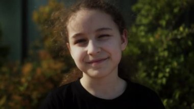Güneş ışınlarındaki mutlu çocuk. Park 'ın yakın plan portresindeki küçük kız yüzü. Rüya gören komik kız. Güneşin altında bir çocuğun mutlu yüzü. Çocuk kameraya gülümser. Yüzü. Parkta mutlu bir çocuk. Güzel bir yüz. 4K