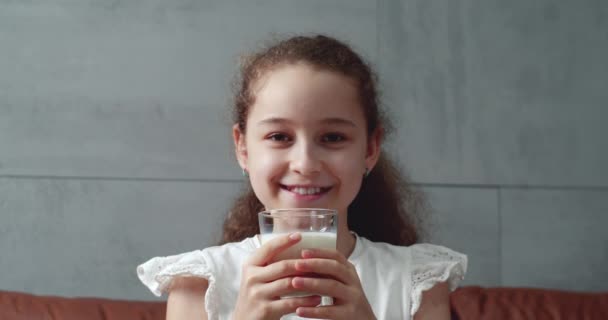 幸せな笑顔の子供はミルクを飲みます 健康的な食事の子供は朝食の子供の夢のコンセプトを食べます リビングルームの女の子はヨーグルトミルクを飲み 彼女の唇をなめる — ストック動画