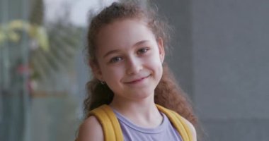 Mutlu bir okul kızının portresi, gülümseyen bir okul kızı, sırt çantalı küçük bir kız, güneşli bir sokakta tek başına duruyor, güzel bir yüz ilkokul öğrencisi 4 bin yaşında.