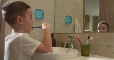 Kafkasyalı çocuk evde aynaya bakıyor. Yaşam tarzı. Portre, banyoda dişlerini fırçalayan ve gülümseyen mutlu bir çocuk. Bebek günlük sağlık hizmeti rutini. 4K.