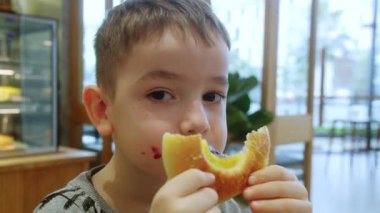 Mutlu çocuk bir kafede reçelli çörek ve süzme peynir yiyor. Bir çocuk için sağlıklı okul kahvaltısı. Aç bir çocuk, içinde süzme peynir olan zengin bir çöreği yer. Öğle yemeği için yemek. Lezzetli hamburger.