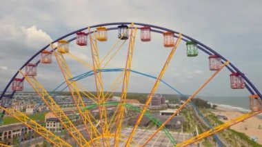 Renkli dönme dolap. Arka planda deniz ve plaj olan bir lunaparkta dönen dönme dolabın havadan görünüşü. Eğlence ve eğlence. Sonsuz döngü. Atlıkarınca eğlendiriyor.