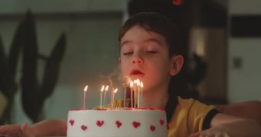 Gözleri kapalı mutlu küçük bir kızın portresi dilek diliyor ve doğum günü pastasına mum üflüyor, çocuk evde doğum gününü kutluyor. Çocuk pastada mum üflüyor..