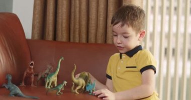 Dinozorculuk oynayan sevimli çocuk komik küçük çocuk. Küçük çocuk evde eğlenen paleontolojiyi anlatıyor. Küçük kardeş çocuklar oturma odasında oyuncak oyunu oynuyorlar. 4K.