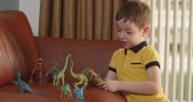 Dinozorculuk oynayan sevimli çocuk komik küçük çocuk. Küçük çocuk evde eğlenen paleontolojiyi anlatıyor. Küçük kardeş çocuklar oturma odasında oyuncak oyunu oynuyorlar. 4K.