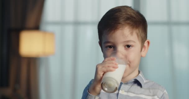 かわいい子供はミルクを飲む 子供が朝食を食べる健康的な子供の夢のコンセプト キッチンの息子の小さな男の子はヨーグルトミルクを飲み 彼女の唇を舐めます — ストック動画