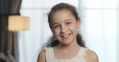 Portre Komik küçük kız kameraya bakıyor evde kanepede oturuyor, güzel yüzlü şirin çocuk kanepede oturuyor. Mutlu bir çocukluk kavramı.