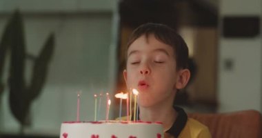 Gözleri kapalı mutlu küçük bir kızın portresi dilek diliyor ve doğum günü pastasına mum üflüyor, çocuk evde doğum gününü kutluyor. Çocuk pastada mum üflüyor..