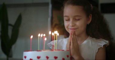 Evde doğum gününü kutlayan bir çocuk. Çocuk pastaya mum üflüyor. Gözleri kapalı, dilek tutan ve doğum günü pastasına mum üfleyen güzel küçük bir kız. 4K.