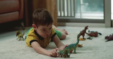 Mutlu küçük çocuklar paleontolojinin evde birlikte eğlenmesini açıklar. Sevgi dolu yetişkin kız kardeş ve tatlı anaokulu erkek kardeşi dinazor oyuncakları oynayarak konuşuyor sıcak zeminde oturuyorlar. 4K.