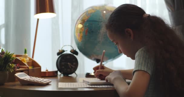 かわいいスマート小学生の女の子の書き込みを学ぶ数学の宿題を書いて自宅のテーブルに座って かわいい小さな就学前の子供だけでノートを作る勉強 子供の小学校の教育の概念 — ストック動画