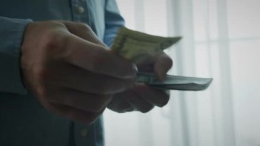 Adam gömleğinin cebinden 100 ve 50 dolarlık banknotlar veriyor, parayı sayıyor, sonra ikiye katlıyor ve gömleğinin cebine koyuyor. Mali yetersizlik, ellerinde dolar banknotları