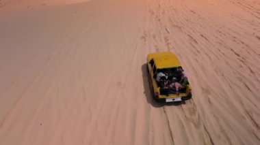 Çölde off-road arabalarla gezen turistlerin, kumlu çölde aşırı jiplerle gezen turistlerin manzarası, yel değirmenlerinin arka planına karşı. 4K.