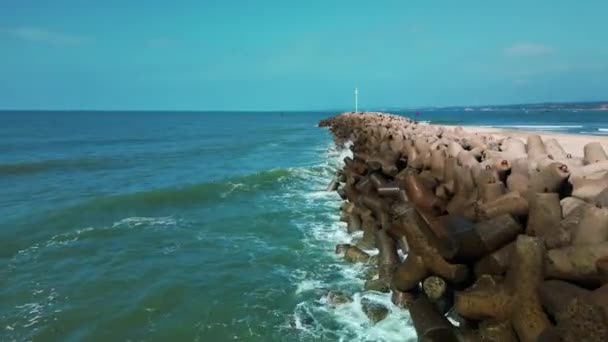 蓝色能量的生命力和清澈的海水 从上方俯瞰五彩斑斓的海水 映衬着海岸线外壮观的防波堤 四脚板上的海浪破裂了 — 图库视频影像