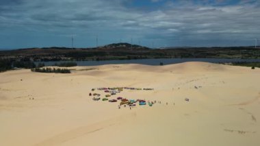 Çölde off-road arabalarla gezen turistlerin, kumlu çölde aşırı jiplerle gezen turistlerin manzarası, yel değirmenlerinin arka planına karşı. 4K.