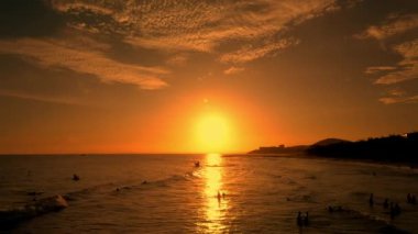 Sörfçüler büyük dalgalarla arka planda güzel bir günbatımına karşı Vietnam denizinde sörf yapar. Sporcular, mutlu insanlar, sörf tahtasında deniz dalgası sürmekten mutlular. İnsansız hava aracından inerek gün batımında deniz arka planında sörf yapıyorlar.