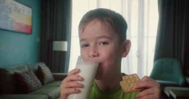 Evde süt içip kraker yiyen yakışıklı bir çocuk portresi. Kahvaltılık çocuk rüyası konsepti yiyen sağlıklı bir çocuk. Mutfaktaki küçük çocuk süt içiyor. Gülümseyen pozitif çocuk