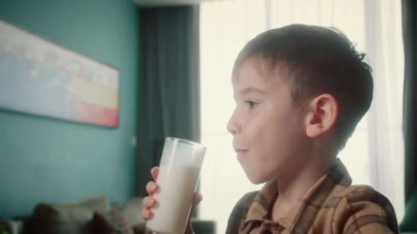 自宅でミルクを飲んでクラッカークッキーを食べるポートレートハンサムな子供 朝食を食べる子供の夢のコンセプトを健康的に食べます キッチンにいる少年は 牛乳を飲んでる ポジティブな子供の笑顔を持っている — ストック動画