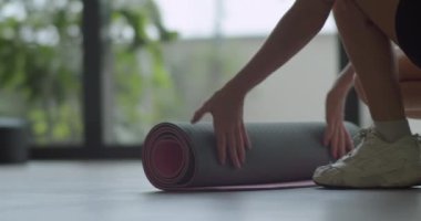 Bir kadının yoga minderini hazırlamak için ikinci çekimini yapın. Paspası açtığınızda görüntüyü kapatın. Genç, formda, sporcu bir kadın. Egzersiz yogası yapıyor..