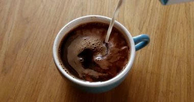 Adding coffee creamer into black coffee. Slow motion cream pouring in a cup of black coffee