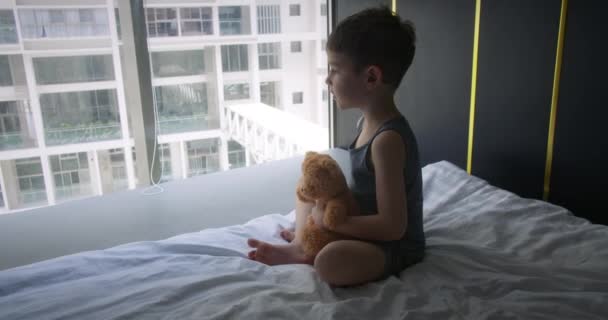 Menino Feliz Bonito Está Sentado Seu Quarto Cama Segurando Urso — Vídeo de Stock