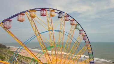 Renkli dönme dolap. Arka planda deniz ve plaj olan bir lunaparkta dönen dönme dolabın havadan görünüşü. Eğlence ve eğlence. Sonsuz döngü. Atlıkarınca eğlendiriyor.