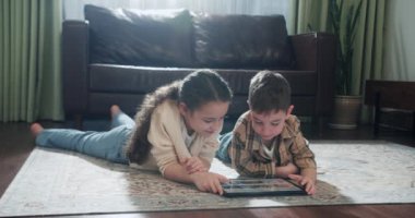 Farklı yaşlardaki sevimli çocuklar dijital cihazlarla, interneti mobil dijital cihazlarla, kız ve erkek çocuk halının üzerinde cep telefonuyla oynuyorlar. 4K.