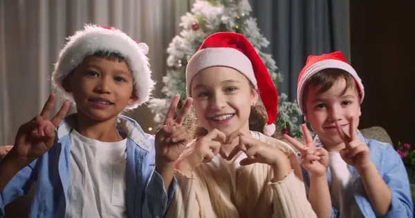 Noel şenliğinde portre çocuğu, Noel Baba şapkalı gülümseyen küçük çocuk koltukta oturuyor arka plandaki dekoratif Noel ağacına bakıyor.