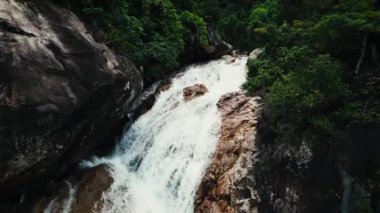 Vietnam 'da inanılmaz güzel bir şelale, suyun yüzeyine düşen sular, çerçevenin önünde devasa taşlar görünüyor. Bereketli yeşil yapraklar rüzgardan, Vietnam 'dan geliyor. 4K.