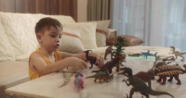 かわいい子供面白い小さな男の子恐竜を再生します 子供は古生物学を家庭で楽しんでいると説明します 子供の小さな兄弟のリビングルームでおもちゃのゲームをプレイ — ストック動画