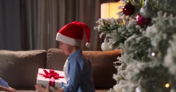 驚きに満ちた幸せなかわいい子供たちは ボックスクリスマスギフトを開き 彼の贈り物から喜びで幸せに落ちます 肖像画の美しい小さな男の子 子供はクリスマスの驚きで箱を開きます — ストック動画