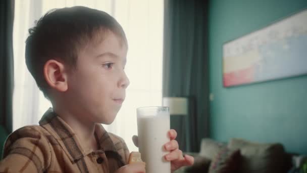自宅でミルクを飲んでクラッカークッキーを食べるポートレートハンサムな子供 朝食を食べる子供の夢のコンセプトを健康的に食べます キッチンにいる少年は 牛乳を飲んでる ポジティブな子供の笑顔を持っている — ストック動画