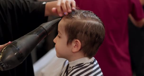 理发师在美容院里用吹风机擦干小孩的头发 高质量的视频 男人小孩的发型和发型在沙龙里 用吹风机吹头发 — 图库视频影像