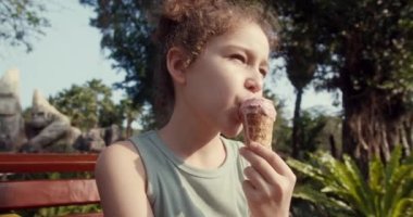 Tatlı bir çocuk yaz boyunca lezzetli bir dondurma külahının tadını çıkarır. Şehir parkında yürüyüş yapan dondurmalı bir çocuk. Dondurma yiyen küçük kızın yakın plan portresi. Çocuk dondurma yalıyor..