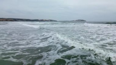 Deniz dalgaları kumlu sahil şeridinde dalgalanırken hiç bitmeyen güzel ve kusursuz görüntülerin drone görüntüsü. Altın plajın, derin mavi okyanus suyu ve köpüklü dalgalarla buluşmasının havadan çekimi. 4K.