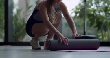 Bir kadının yoga minderini hazırlamak için ikinci çekimini yapın. Paspası açtığınızda görüntüyü kapatın. Genç, formda, sporcu bir kadın. Egzersiz yogası yapıyor..