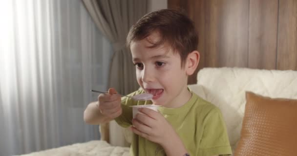 开心的微笑孩子喝牛奶 健康饮食儿童吃早餐儿童梦想的概念 客厅里的儿子小男孩喝酸奶牛奶 舔她的嘴唇 积极的孩子笑着吃早饭 — 图库视频影像