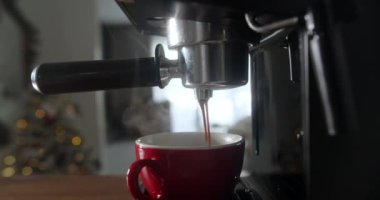 Makineden fincana dökülen bir rulo kahve. Ev yapımı sıcak kapuçino bir Noel ağacı ve Noel ışıklarına karşı. Taze öğütülmüş kahve akar. Sabahları içerim.