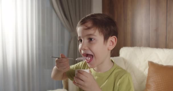笑顔の子供がミルクを飲んでいる 朝食を食べる子供を健康的に食べる子供の夢の概念 リビングルームの息子はヨーグルトミルクを飲んで唇を許可する ポジティブな子供 朝食を持っている — ストック動画