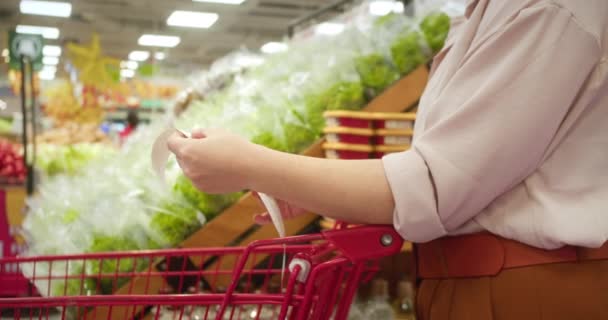Frau Überprüft Einkaufswagen Frau Vor Dem Hintergrund Des Gemüses Überprüft — Stockvideo