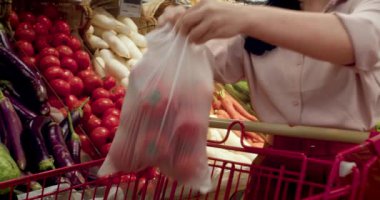 Güzel, genç, esmer, güzel bir kadın marketten yiyecek, domates alıyor. Kız ürünleri, sebzeleri, meyveleri dükkandan seçiyor. Alışveriş, vegan satış konsepti. 4K