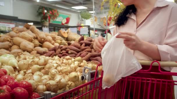 女人在杂货店里买洋葱 在超市里买东西 在市场上买东西 选择洋葱 女孩子拿着袋子在篮子里买蔬菜 蔬菜洋葱妇女的手 — 图库视频影像