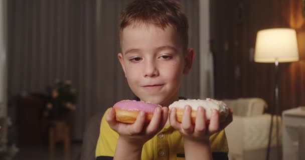 食生活障害のある白人子供は すぐに2つのドーナツを同時に食べたいと考えており どのドーナツを最初に食べるかを決めることはできません 学校の少年は2つのドーナツを同時に食べている 甘い中毒コンセプト 4Kについて — ストック動画