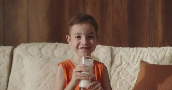 Malý Chlapec Pozitivní Dítě Pije Mléko Zatímco Sedí Doma Pohovce Royalty Free Stock Obrázky