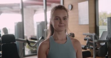 Bir fitness kızı portresi, spor salonunda kız kameraya olumlu bir şekilde bakıyor. Spor salonundaki spor eğitimine olumlu yaklaşım. Spor kulübündeki kadın. 4K