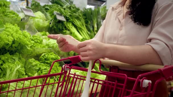 野菜のバックグラウンドに反対する女性は 食料品カートにDear Amount請求書をチェックして モールで食料品の買い物の後に紙チェックをチェックします 食品価格の増加 食料品店のカートを点検する女性 — ストック動画