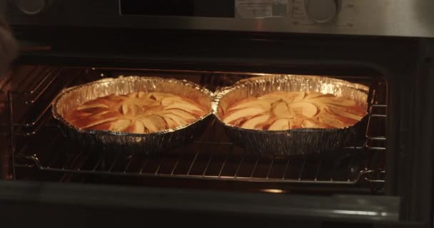 一名年轻女子的特写镜头 打开烤箱 取出两个苹果馅饼在一个铝箔烤盘与面团 家庭主妇烘焙概念 妇女准备苹果馅饼 — 图库视频影像