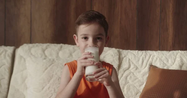 Der Kleine Junge Trinkt Milch Während Hause Auf Dem Sofa lizenzfreie Stockfotos