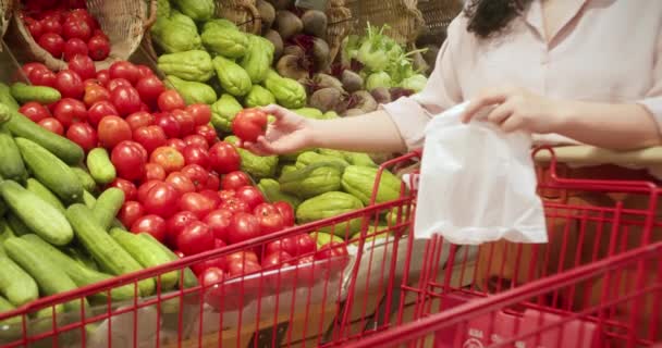 かなり若い美しいブルネットの髪の女性は スーパーマーケットで食べ物 トマトを買います 女の子は店で製品 果物を選びました ショッピング ビーガンセールスコンセプト — ストック動画